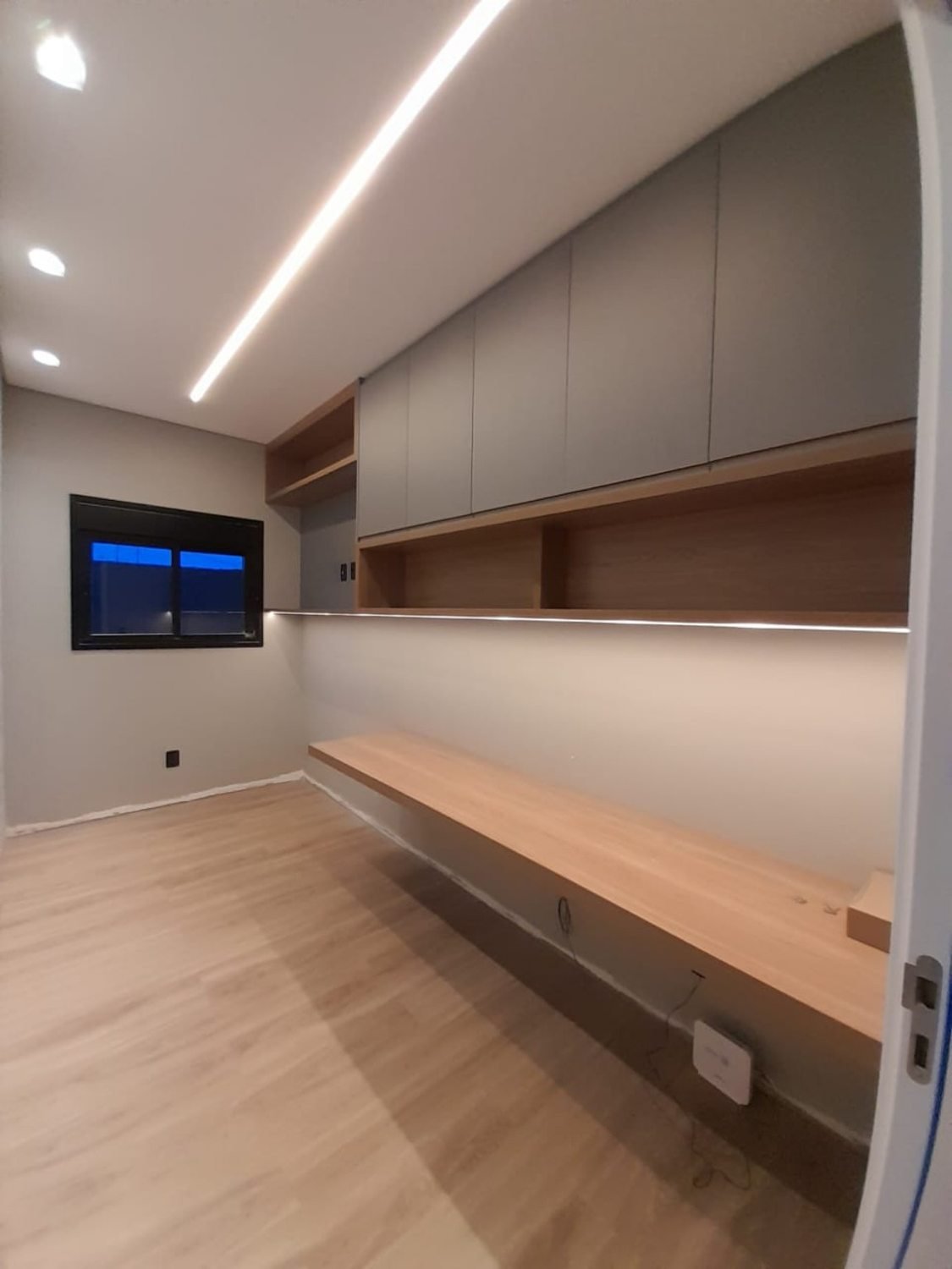 Home office com bancada longa e armários com iluminação LED